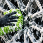 Professional detailer cleaning a custom brushed forged wheel using a soft microfiber mitt and rich soap foam.